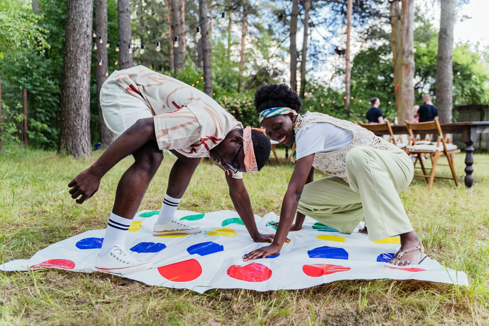 Two friends enjoying a game of Twister outside on a sunny day, surrounded by nature.